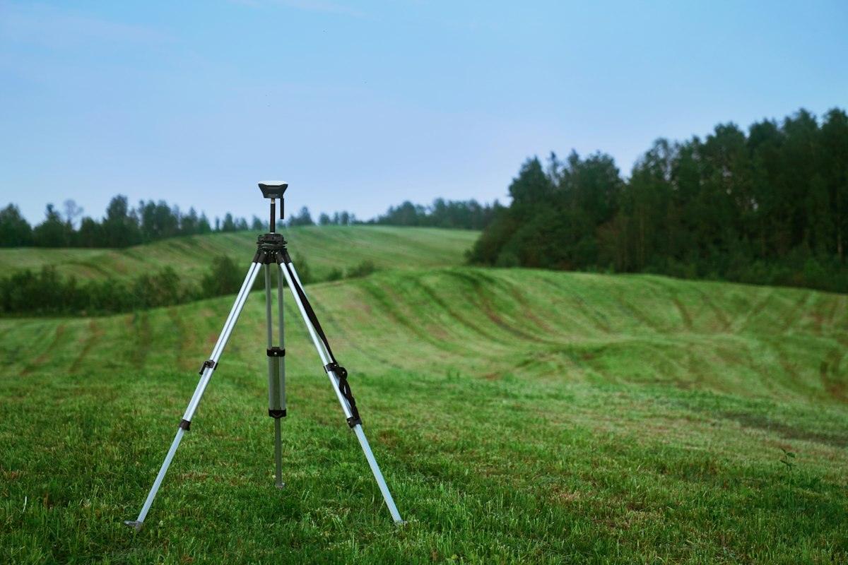 A survey instrument on a tripod in a green field